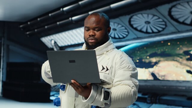 Astronaut in spacecraft using laptop to run telemetry data analysis. Man in spaceship wearing spacesuit analyzing mission logs on notebook during planetary exploration, camera B