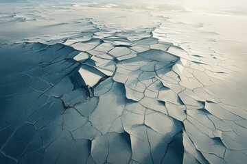 Aerial view of cracked glacial ice with contrasting blues and whites, conveying fragility and climate change.