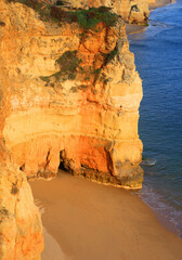  Lagos, Algarve, Portugal. Golden cliffs with an empty wet sandy secluded beach. Late afternoon sunlight.