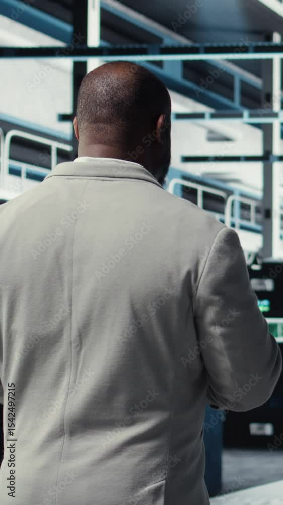 Poster vertical video employee walking in server farm, analyzing equipment metrics on device screen. africa