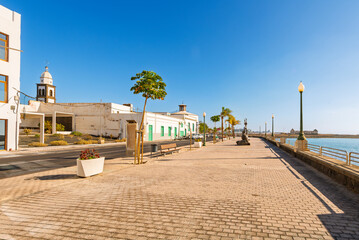 The seaside promenade and boardwalk with the bell tower of San Gines Church behind whitewashed buildings in Arrecife, Spain, Canary Islands.