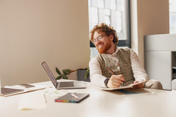 A cheerful man is brainstorming innovative ideas in a stylish and modern workspace equipped with a...