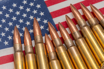 Obraz premium Firearms cartridges arranged in a row on the background of the American flag. The image symbolises guns, patriotism, the right to self-defence and military themes in the USA.