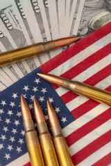Close-up of firearm ammunition lying on an American flag with blurred dollar notes in the background. The image symbolises the themes of war, security, power and financial influence in the USA.
