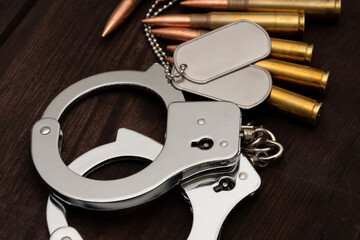 A close-up of shiny handcuffs, two army badges and several cartridges. The objects are lying against a background of aged wood,