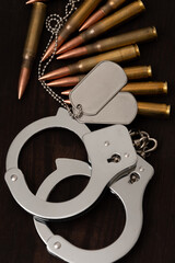 Symbolic combination of handcuffs, tokens and bullets on a dark wooden background. Suitable for illustrating the concepts of war, peace, crime, punishment and defence.
