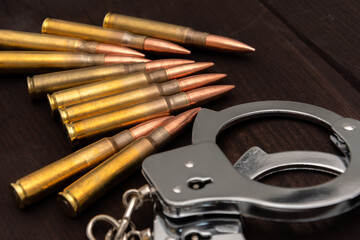 Metal handcuffs and a row of rifle cartridges lying on a dark wooden surface. The image symbolises the themes of crime, justice, danger and punishment.