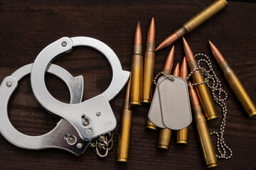 Obraz premium Metal handcuffs, army badges and rifle cartridges are arranged on a dark wooden surface. The image symbolises the themes of justice, military service, crime and conflict.