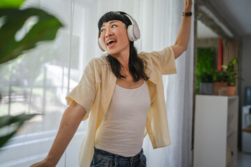Playful japanese woman listen music on headphones and dancing at home