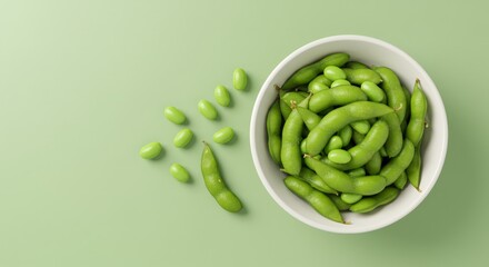 Top view of fresh green edamame beans in a white bowl with some scattered pods and soybeans on a pastel green background. Healthy plant-based protein snack or appetizer