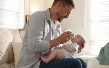 Father feeding his little baby with bottle on sofa at home