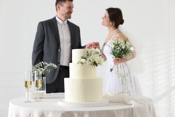 Happy married couple together indoors, focus on wedding cake on table