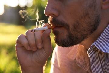 Man smoking cigarette on blurred background, closeup