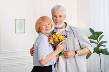 Lovely senior couple with bouquet of flowers at home