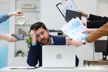 Man overwhelmed by different requests from colleagues at desk in office