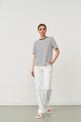 Beautiful female model poses in stylish striped top and white pants in studio setting