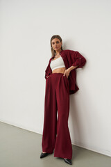 Woman in burgundy wide-leg pants and matching shirt, wearing a white crop top and black heels,...
