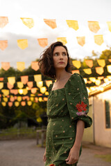 Fototapeta premium Young woman with short hair and green dress standing alone in old town square with flags in background