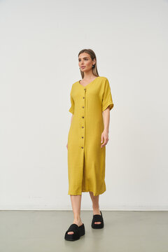 Woman in yellow dress with buttons, short sleeves, standing on light floor, wearing black platform sandals, looking forward, minimal style, casual fashion, neutral expression