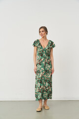 Woman wearing a green leafy-patterned dress stands confidently, hands relaxed by sides. Her hair is...