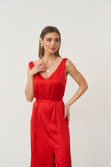 Woman in a sleeveless red dress with a tied waist, looking to the side. She has straight,...