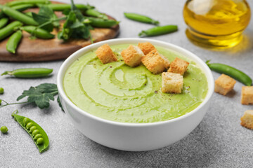 Tasty pea cream soup with croutons served on grey table, closeup