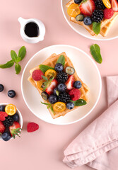 Crispy Belgian waffles with fresh berries and maple syrup on pink background. Top view.