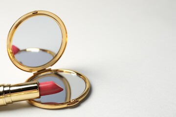 Open pocket mirror and lipstick on light grey background, closeup. Space for text