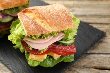 Tasty baguette sandwich with ham and vegetables on wooden table, closeup