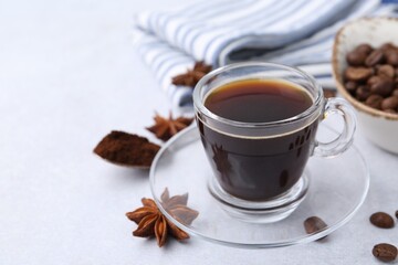 Cup of aromatic coffee, beans and star anise on white table, closeup. Space for text