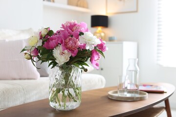 Bouquet of beautiful peonies and water on coffee table indoors. Interior design