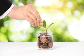 Investment for future profit. Woman putting coin into glass jar with seedling on white table...