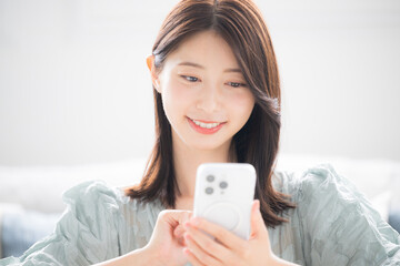 部屋でスマホをタップする若い女性の春夏の半袖の上半身のクローズアップ
