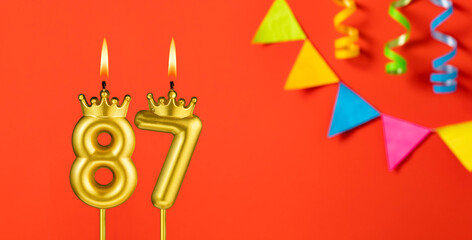 Number 87 candle - Birthday celebration on an orange background with pennants