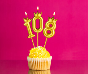 Yellow birthday cupcake with a number 108 candle - Birthday card on a pink background