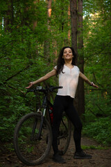 Beauty smiling sport free woman biking on bicycle on path among green woods in a summer forest...