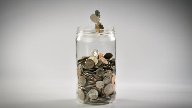 Close-up shot of coins falling into a coin jar in slow motion.