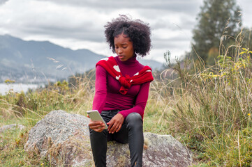 Young woman using smartphone sitting on rock in nature