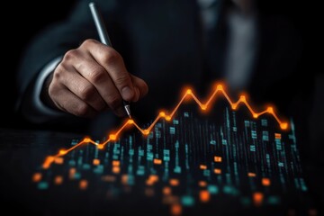 Hand holding pen drawing glowing orange financial graph line over digital data visualization on dark background symbolizing growth and analysis