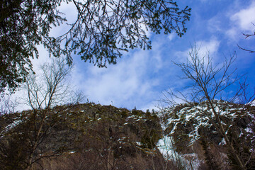  Beautiful winter mountain landscape with snow-covered cliffs, icy waterfall, evergreen trees, and blue sky with clouds. Perfect for themes of nature, wilderness, adventure, and winter travel.