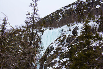  Frozen waterfall cascading down a rocky mountain slope covered with snow and ice. Winter...