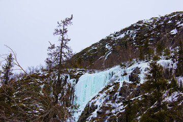  Frozen waterfall cascading down a rocky mountain slope covered with snow and ice. Winter...