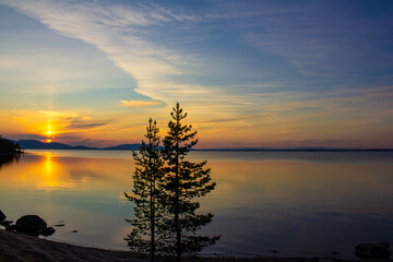  Beautiful sunset over calm lake with pine trees, colorful sky, and reflections in still water. Scenic peaceful landscape ideal for backgrounds, travel, relaxation, meditation, banners, and designs.