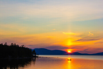 Obraz premium Breathtaking lake sunset with glowing sun over mountains, tranquil water, and dramatic colorful sky. Perfect for travel, inspiration, nature backgrounds, relaxation, and peaceful mood scenes.