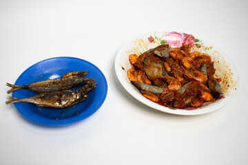 A simple home cooked meal featuring two seafood dishes of fried fish and chili prawns served on a blue plate.
