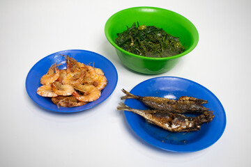 A dish of fried prawns, fried fish and a bowl of green vegetables.