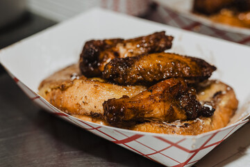 Close-up of glazed chicken wings resting atop French toast dusted with powdered sugar in a paper...