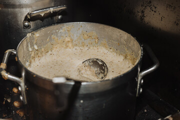 Large stainless-steel pot of creamy grits with seasoning flecks and a ladle resting inside in a...