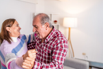 Happy senior couple dancing together at home in living room