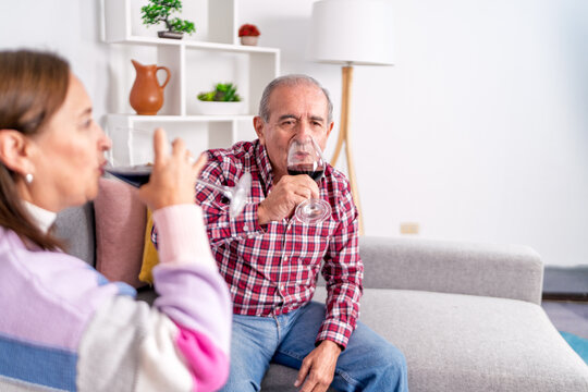 Senior couple enjoying red wine together on sofa at home - Powered by Adobe